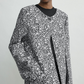 Model wears Toteme’s Collarless Floral Coat—black and white jacquard with round neckline, large button, and pockets—against a plain light background. Ideal for an elevated occasion look.