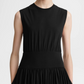 A person wearing the Toteme Sleeveless Cotton Tee Dress, a black organic-cotton jersey dress with a fitted waistband and gathered skirt, is photographed from the shoulders to just above the knees against a plain background.