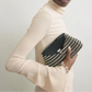 A person in a long-sleeved, textured beige dress holds Toteme's Mini T-Lock Woven Clutch against a plain light background.