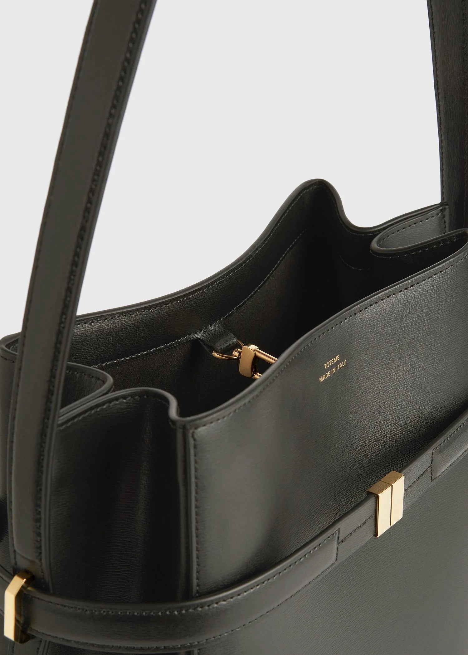 Close-up of a black Toteme Belted Bucket Bag with gold hardware and visible internal compartments, showing the "TOTEME MADE IN ITALY" stamp.