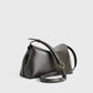 Toteme's T-Lock Clutch is a minimalist structured shoulder bag in dark Palmellato leather, featuring an adjustable strap and a gold T-Lock buckle, shown against a plain light background.