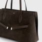The Suede Lounge Tote by Toteme is a large, dark brown Italian suede bag with two top handles and a minimalist design, featuring a subtle metallic accent—ideal for everyday use.