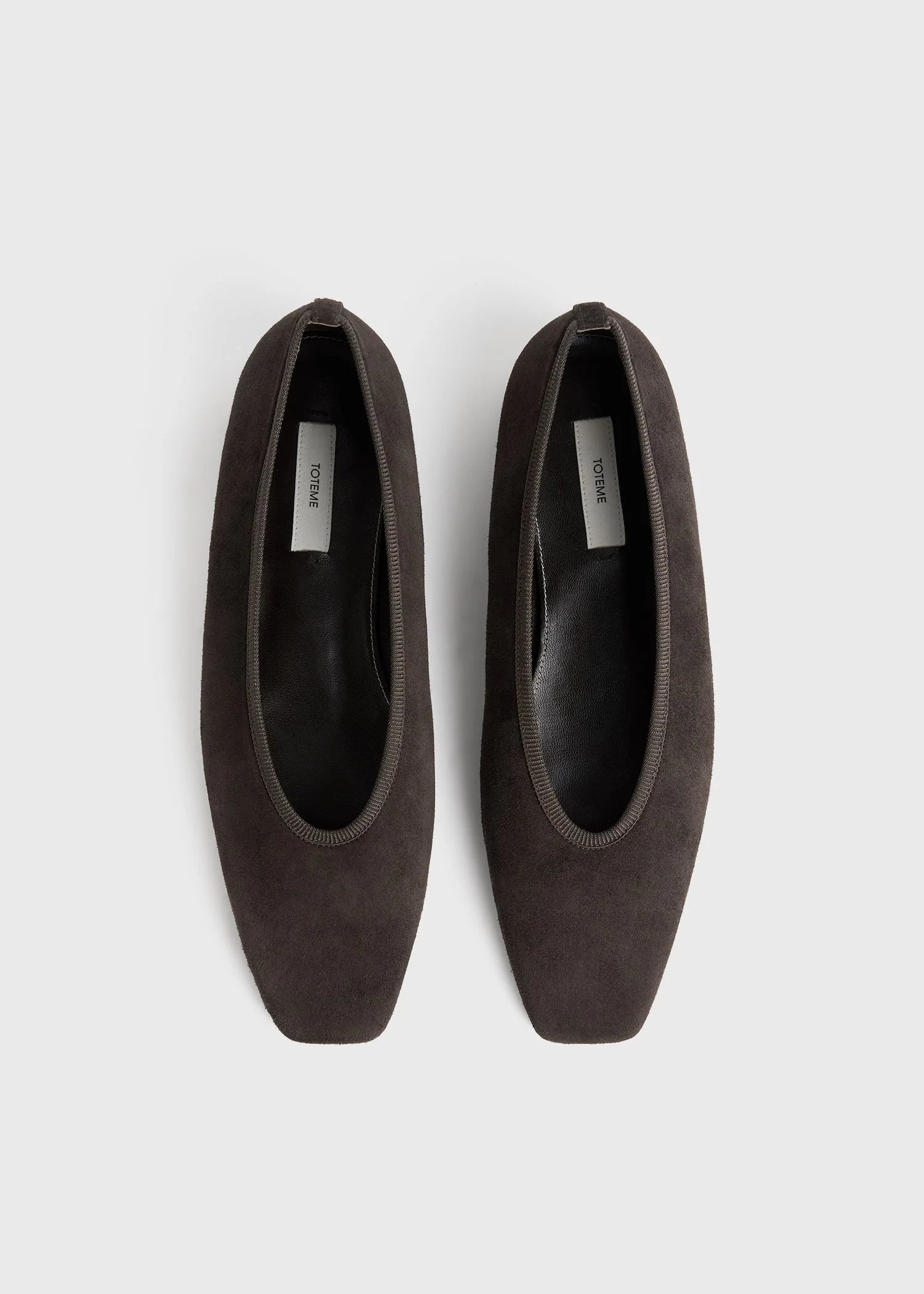 A pair of Toteme Minimalist Suede Ballerinas in dark brown with square toes, made in Spain, shown from above on a plain white background.
