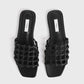 A pair of Toteme Braided Leather Bandeau Slides in black with flat soles, open toes, braided knotted leather straps, and square toes, shown on a white background.