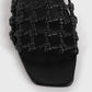 Close-up of Toteme's Braided Leather Bandeau Slides in black, showcasing a braided, knotted lattice upper and square toe against a light background.