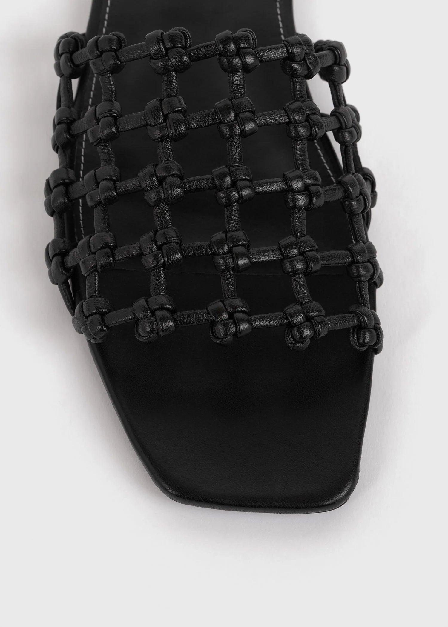 Close-up of Toteme's Braided Leather Bandeau Slides in black, showcasing a braided, knotted lattice upper and square toe against a light background.