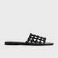 The Braided Leather Bandeau Slides by Toteme feature a black, flat design with an open, braided leather upper and thin sole, shown on a light gray background—an elegant update to classic Toteme slides.