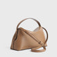 The Toteme T-Lock Top Handle Bag in tan Palmellato leather has a structured silhouette, signature T-Lock closure, top handle, and adjustable shoulder strap, shown against a plain light background.