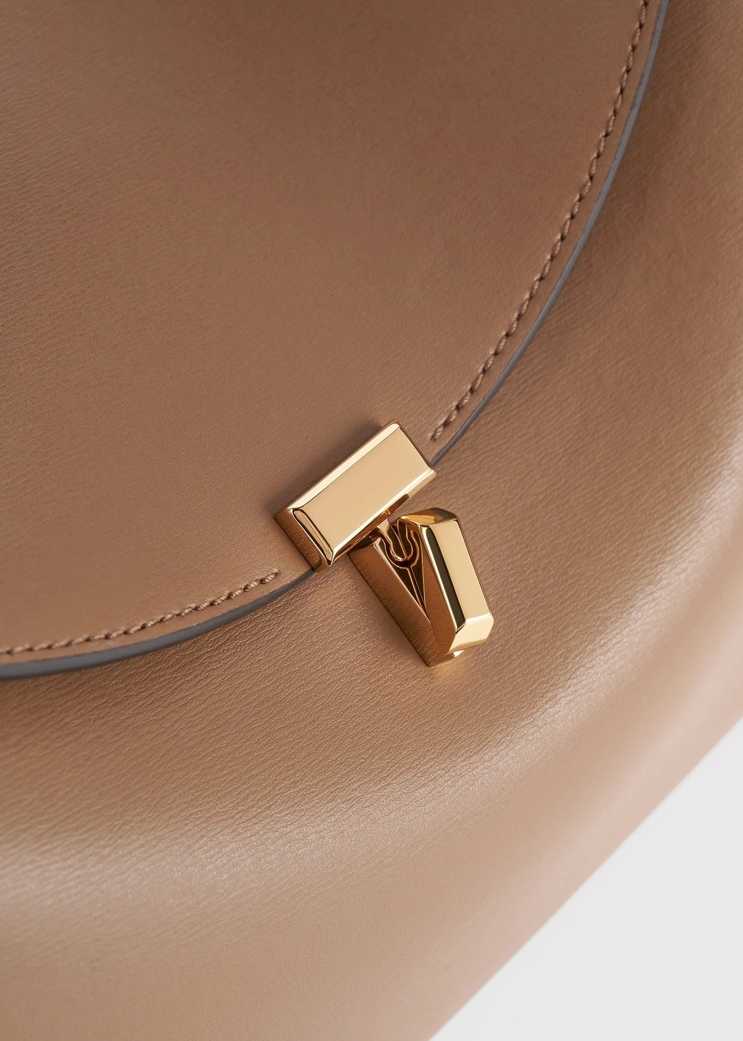Close-up of the Toteme T-Lock Top Handle Bag in tan Palmellato leather, showcasing a gold rectangular T-Lock clasp on the front flap.