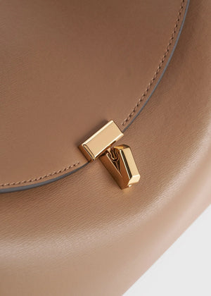 Close-up of the Toteme T-Lock Top Handle Bag in tan Palmellato leather, showcasing a gold rectangular T-Lock clasp on the front flap.