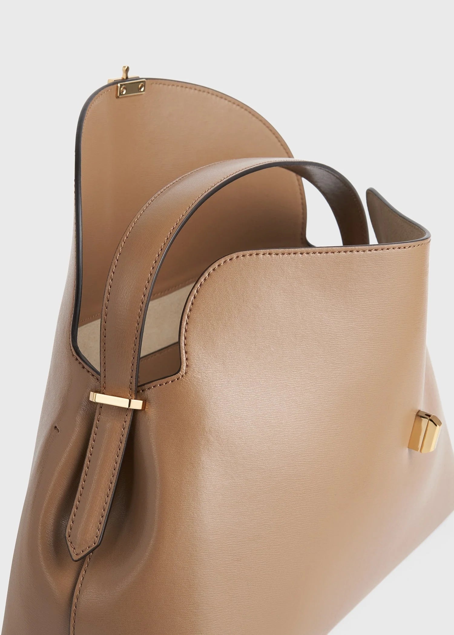 A close-up of Toteme's T-Lock Top Handle Bag in tan Palmellato leather with gold hardware, featuring one handle, an open top, and a beige interior lining.