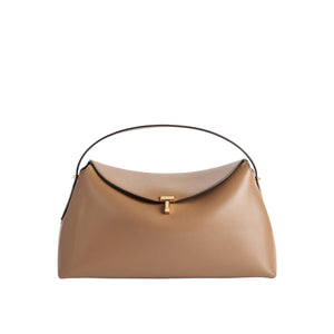 The Toteme T-Lock Top Handle Bag is crafted from tan Palmellato leather with a curved top flap, gold T-Lock clasp, and single black handle, displayed against a white background.