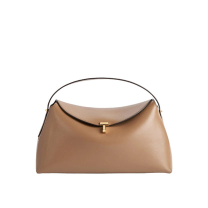 The Toteme T-Lock Top Handle Bag is crafted from tan Palmellato leather with a curved top flap, gold T-Lock clasp, and single black handle, displayed against a white background.