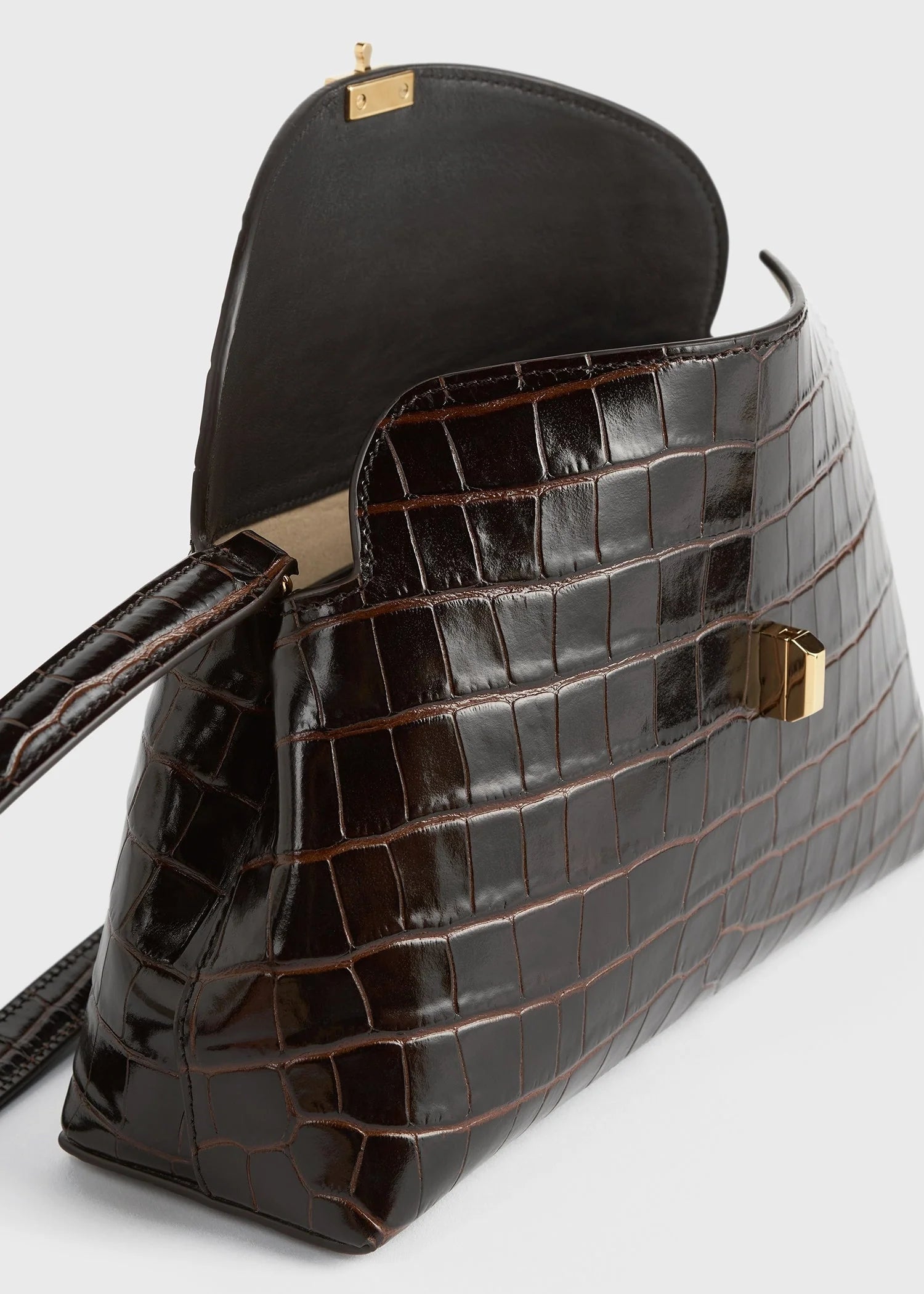 The Toteme T-Lock Embossed Croc Clutch is a dark brown crocodile-effect bag with a gold T-Lock clasp and a partially open flap, hinting at its interior.