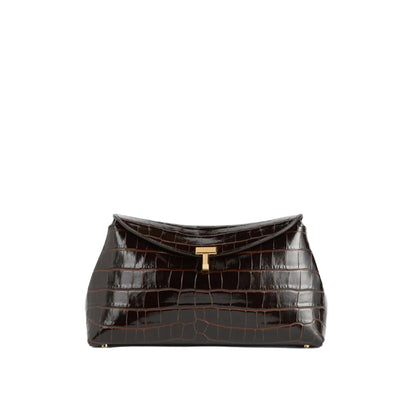 The Toteme T-Lock Embossed Croc Clutch in dark brown features crocodile-effect leather and a gold-tone T-Lock clasp, shown against a plain white background.