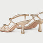 The Loeffler Randall Triana Mid Heel Sandal is featured here in a striking metallic gold finish, showcasing delicate straps, a square toe, and a chic mid-height heel against a plain light background. This elegant design brings a contemporary edge to the timeless strappy sandal silhouette.