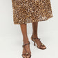 A person wears a leopard print skirt and Loeffler Randall Triana Mid Heel Sandals in brown nappa leather, standing on a white floor against a white background.