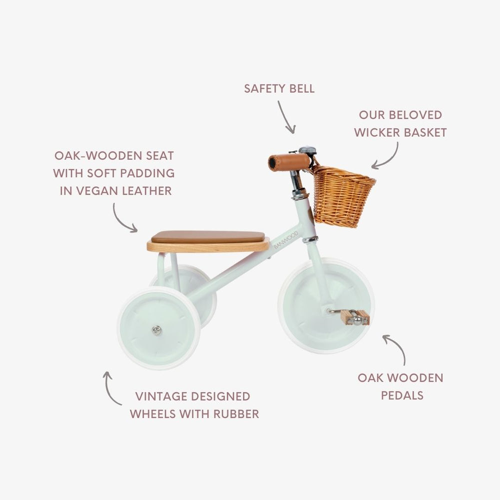 Introducing the Banwood Kids’ Trike: a white children’s tricycle with a sturdy oak wooden seat and pedals, safety bell, vintage-style rubber wheels, and an adorable wicker basket adorning the handlebars. Each detail of this beautifully crafted classic trike is thoughtfully designed to combine charm, comfort, and safety for young riders.