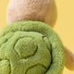 Close-up of Jellycat's Thimble Turtle, the ideal adventure companion, highlighting its soft green shell and brown body against a cheerful yellow background.