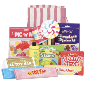 A variety of colorful toy food packaging, including items labeled "Chocolate Spirals," "Rainbow Stars," and "Teeny Tinys," with a striped bag in the background, all part of the Le Toy Van Sweet & Candy Set by Le Toy Van featuring pieces made from sustainable rubberwood.