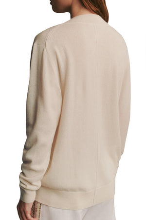 Rear view of a person wearing a TWP Deep V Cashmere Sweater in plain beige with a ribbed cuff and collar.