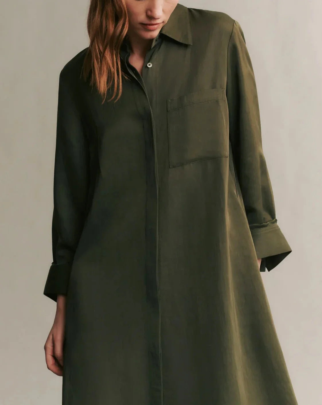 A person wearing TWP's Jenny's Coated Linen Gown, a long-sleeve olive green shirtdress featuring a front pocket and a point collar.