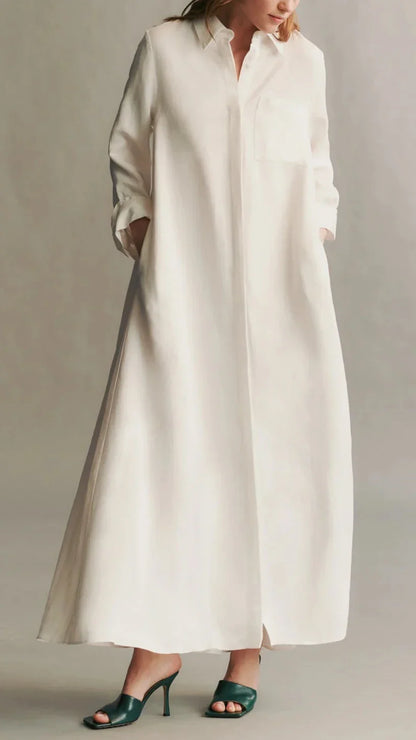 Person wearing the TWP Jenny's Coated Linen Gown, a long sleeve shirtdress with a point collar in white, hands in pockets, and green high heels, standing against a neutral background.