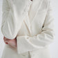 A woman in an elegant TWP Husband Linen Jacket with notched lapels, her arms crossed, close-up view focusing on the outfit detail.