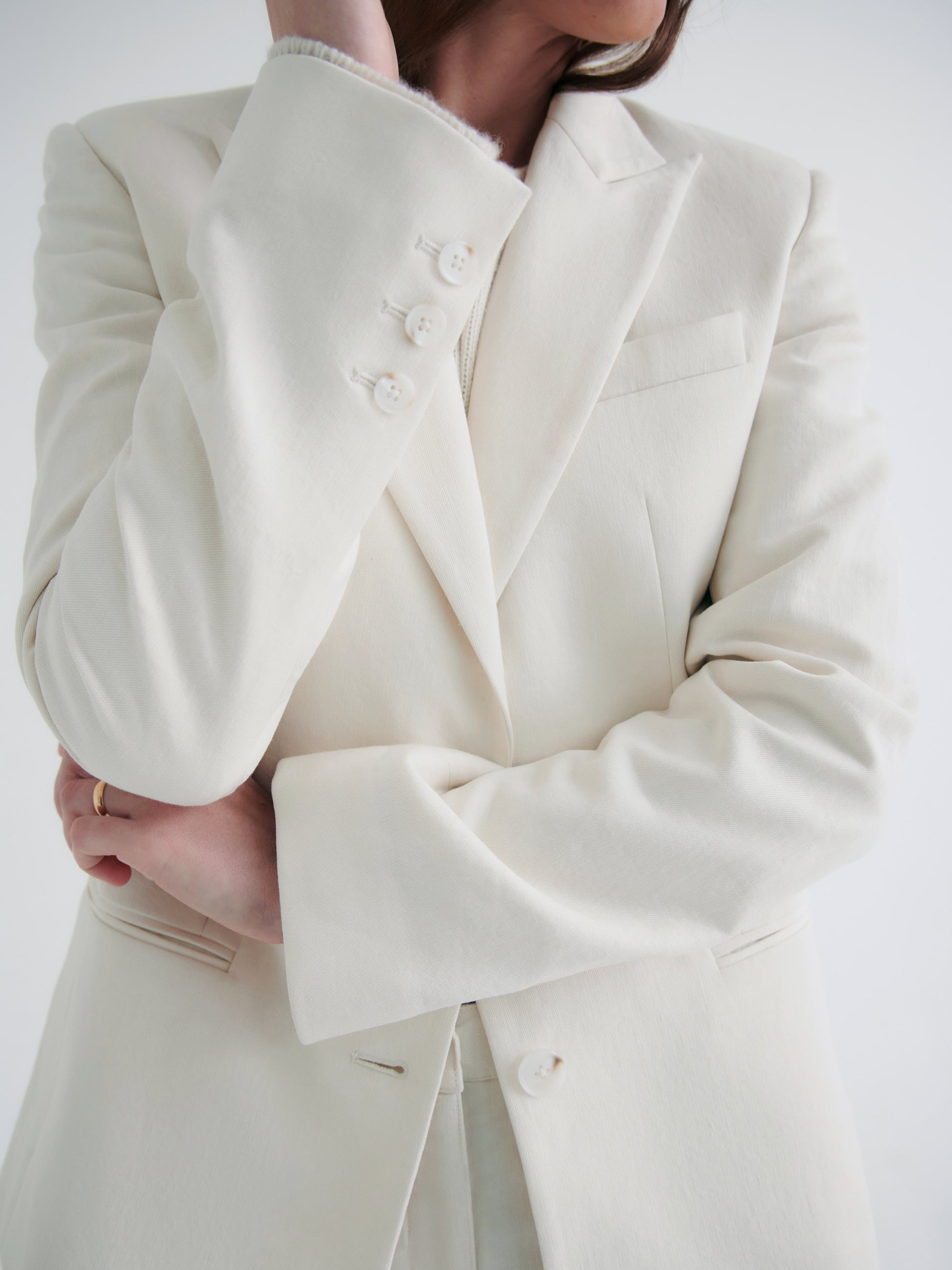 A woman in an elegant TWP Husband Linen Jacket with notched lapels, her arms crossed, close-up view focusing on the outfit detail.