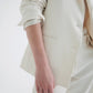 Close-up of a person’s arm in a TWP Husband Linen Jacket blazer and trousers against a white background.