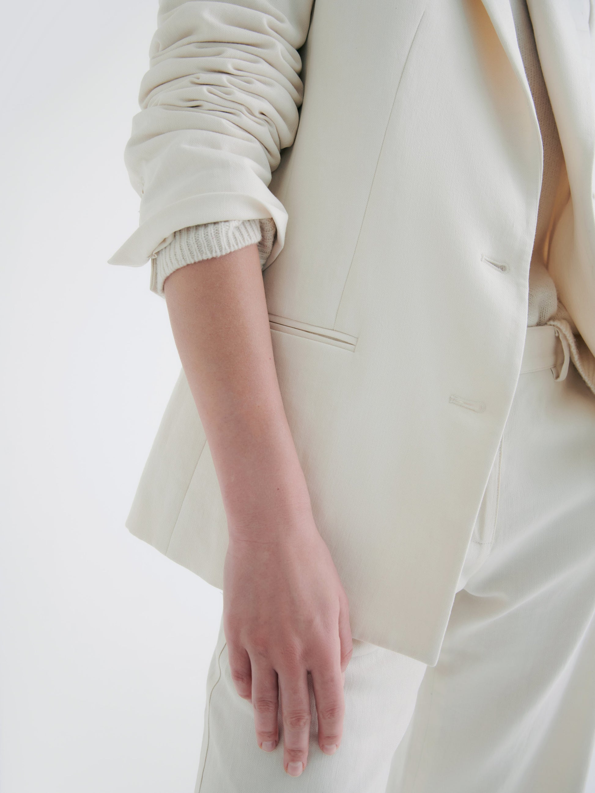 Close-up of a person’s arm in a TWP Husband Linen Jacket blazer and trousers against a white background.