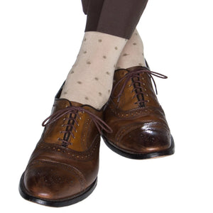 A person wearing brown dress shoes, Dapper Classics Dot Cotton Mid Calf Socks in light beige, and brown pants, crossing their legs.