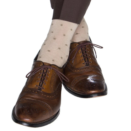 A person wearing brown dress shoes, Dapper Classics Dot Cotton Mid Calf Socks in light beige, and brown pants, crossing their legs.