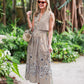 A woman stands on a garden path wearing the Lela Rose Collared V-Neck Dress, paired with sunglasses, sandals, and holding a woven handbag.