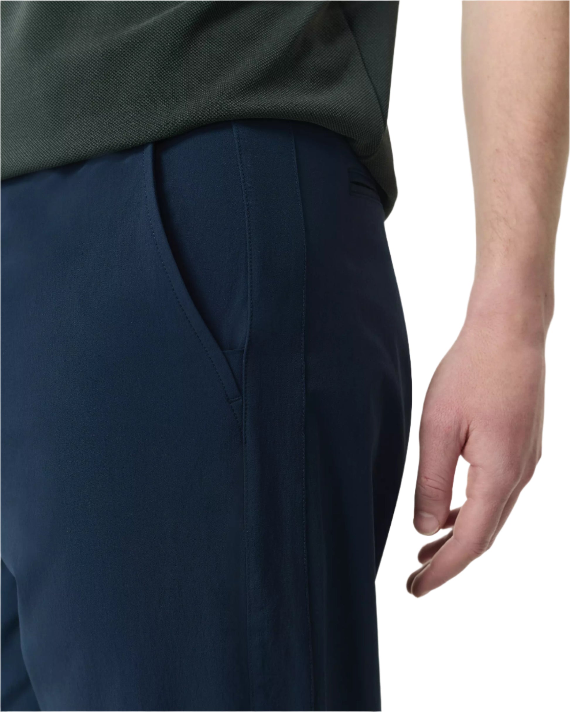 A close-up of a person wearing Rag & Bone’s Tapered Nylon-Blend Trouser in dark blue, paired with a dark green shirt, their right hand relaxed by their side.