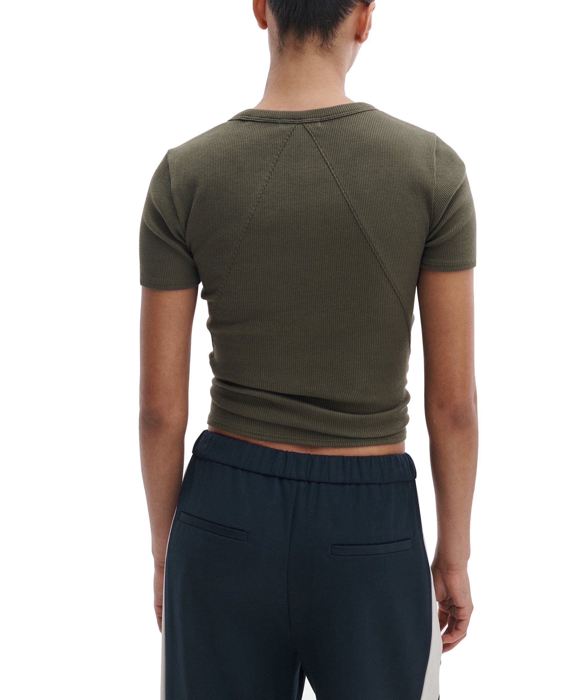 Model shown from the back in Rag & Bone's Essential Ribbed Tee, fitted and short-sleeved in olive green, paired with navy blue pants with white side panels—timeless wardrobe staples against a white background.
