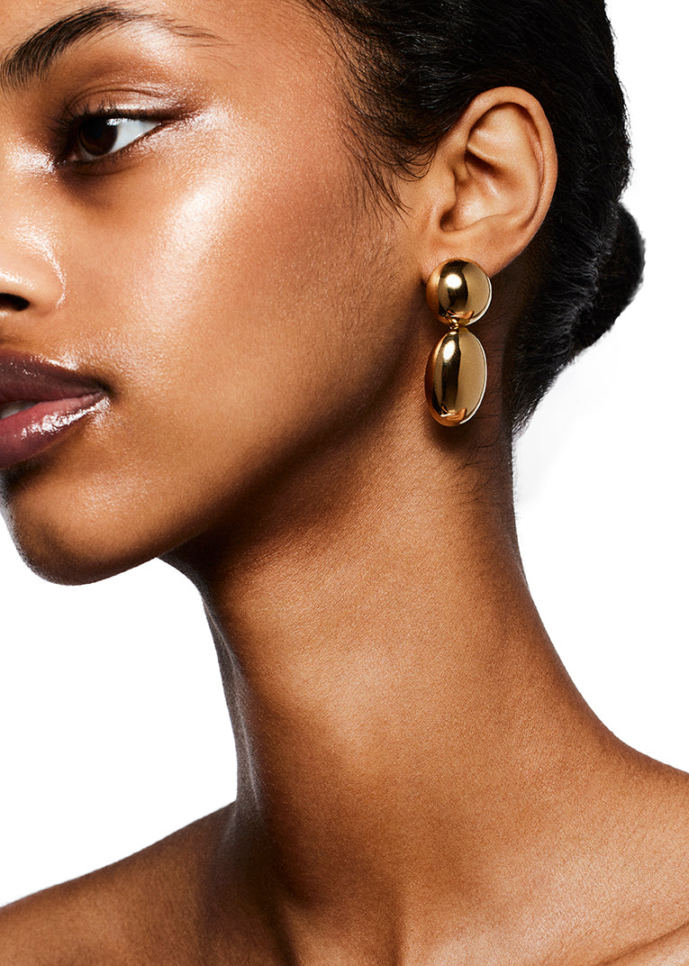 Close-up of a person wearing the LIÉ STUDIO Klara Earrings by Lie Studio. They have a smooth complexion and their hair is pulled back, creating an antique silhouette against the white backdrop.