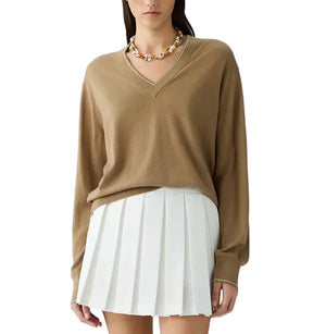 A woman wears The Airy V lightweight cashmere V-neck sweater by Guest in Residence—perfect for summer layering—paired with a chunky beaded necklace and a white pleated mini skirt.