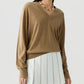 A person wearing The Airy V lightweight cashmere V-neck sweater by Guest in Residence, paired with a white pleated skirt and a beaded necklace, standing against a plain background.