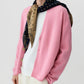 A person wearing The Wild Rag reversible paisley scarf by Guest in Residence, draped over their shoulders, styled with a pink cardigan over a white t-shirt and cream pants.