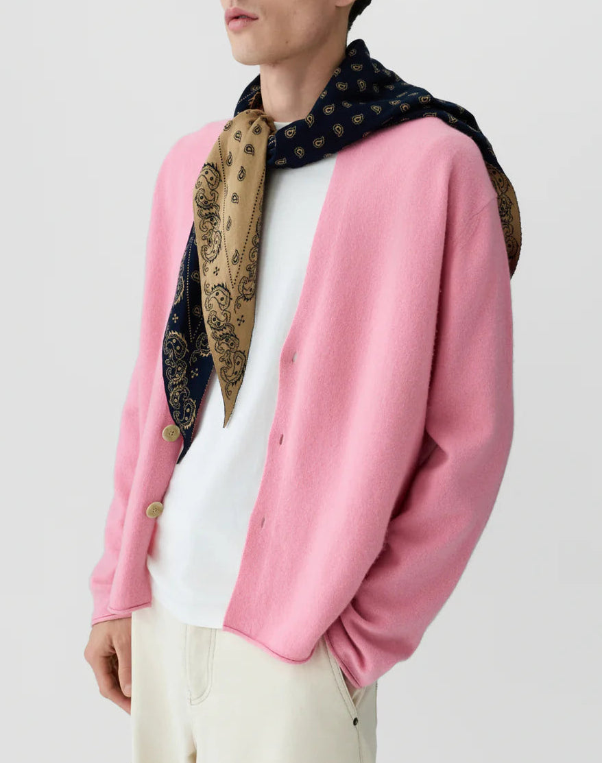 A person wearing The Wild Rag reversible paisley scarf by Guest in Residence, draped over their shoulders, styled with a pink cardigan over a white t-shirt and cream pants.