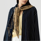 A woman wears a navy pinstripe shirt over a beige top, with The Wild Rag by Guest in Residence—a tan and navy reversible paisley jacquard scarf—draped over her shoulders and knotted at the front.
