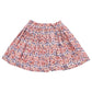 The Pink Chicken Girls' Theodore Skirt from Pink Chicken is a knee-length skirt featuring a colorful floral pattern in shades of red, pink, blue, and white. It boasts an elastic ruffle waist adorned with shimmery rose gold thread.