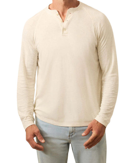 A man wearing a cream Faherty Long-Sleeved Cloud Henley and light blue jeans, standing against a white background.
