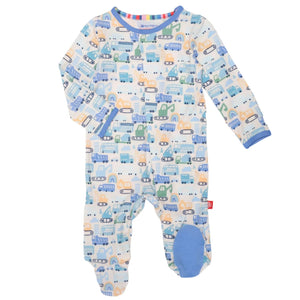 Introducing the Magnetic Me "As Truck Would Have It" Footie, a delightful baby romper showcasing a vibrant vehicle pattern with cars and trucks in shades of blue, orange, and green. Made from temperature-regulating TENCEL™ modal, this footie features convenient magnetic closures along with blue footies and cuffs for added comfort.