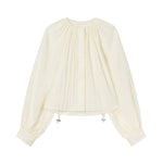 The Gathered Shirt by CO is a long-sleeved, off-white blouse featuring front pleats, a round-neck silhouette, buttoned cuffs, and an adjustable toggle drawstring hem for a custom fit.