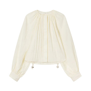 The Gathered Shirt by CO is a long-sleeved, off-white blouse featuring front pleats, a round-neck silhouette, buttoned cuffs, and an adjustable toggle drawstring hem for a custom fit.