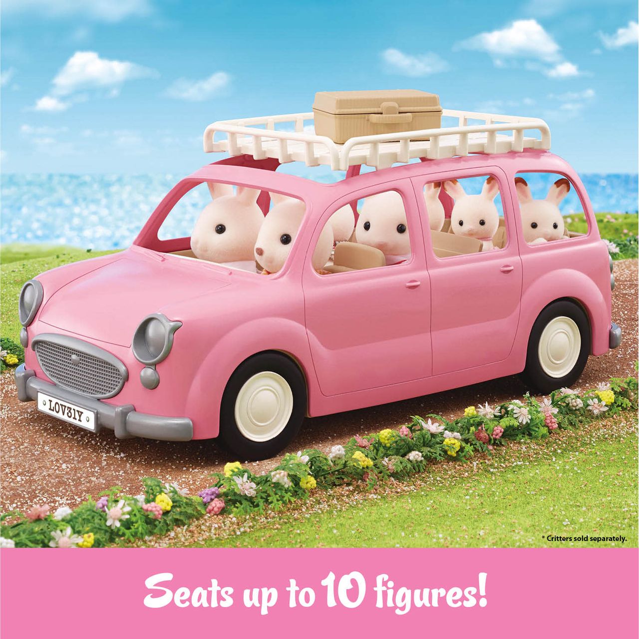 Four Calico Critters rabbit figures ride in the Calico Critters Family Picnic Van, which features a pink design, roof rack, and suitcase. They’re driving along a seaside path under a blue sky, ready for adventure with their picnic accessories.