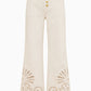 Lou Eyelet Jean by Ulla Johnson: High-waisted white flared denim pants adorned with gold buttons and laser-cut paisley detailing at the hem, finished with delicate eyelet embroidery for a vintage-inspired look.