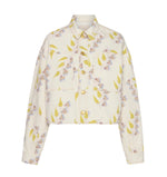 The Bobbi Cropped Denim Jacket by Ulla Johnson is a collared, button-front jacket with long sleeves and a subtle floral and leaf print on cream—an elegant, modern piece for any outfit.
